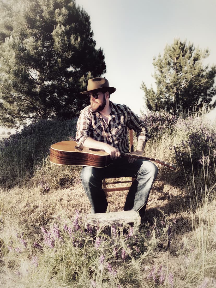 Sean Anthony Sullivan sits in brush with guitar.
